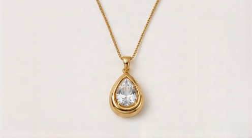 A gold teardrop pendant necklace with a clear teardrop gemstone, displayed on a clean off-white background.
